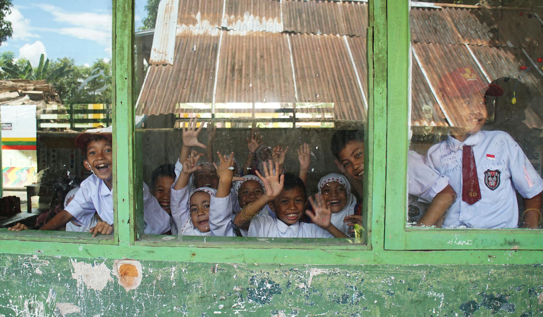 children smiling and waving from behind a school window